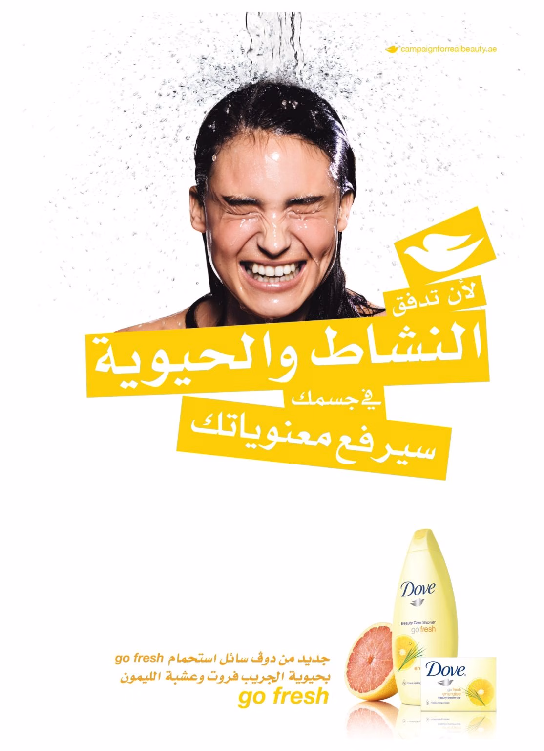 Una donna sorridente sotto l'acqua che schizza, accanto a una scritta in arabo di colore giallo acceso e ai prodotti per il corpo Dove Go Fresh con una fetta di pompelmo.