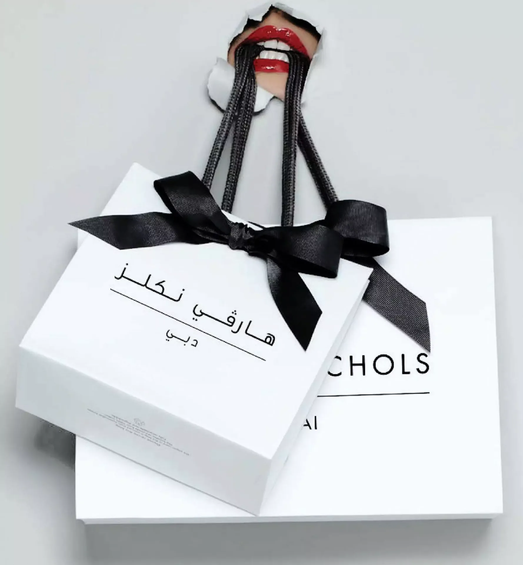 Close-up of a white Harvey Nichols gift bag tied with a black bow ribbon and Arabic calligraphy text