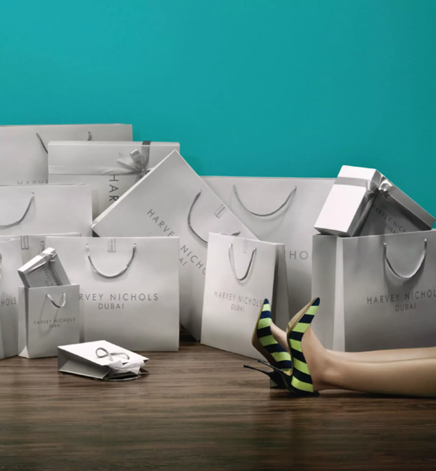 Collection of luxury light grey Harvey Nichols shopping bags with ribbon handles set against a teal background