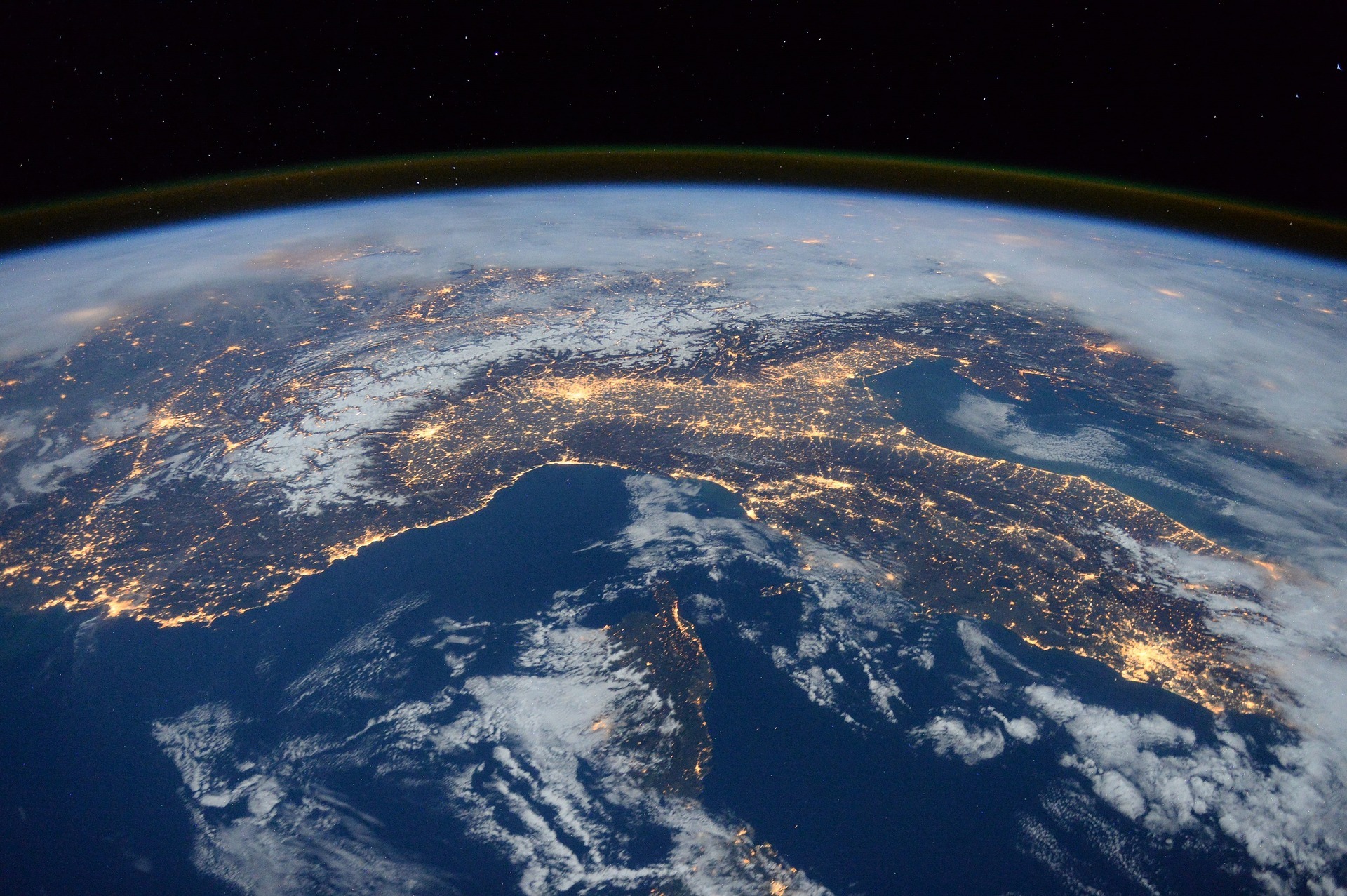 Panoramic satellite view of Earth at night showing glowing illuminated city lights across Europe and the Mediterranean peninsula against the curvature of the planet.
